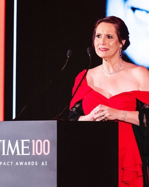 Kay Firth-Butterfield speaking at a podium in a red dress, a TIME100 Impact Awards AI sign beside her.