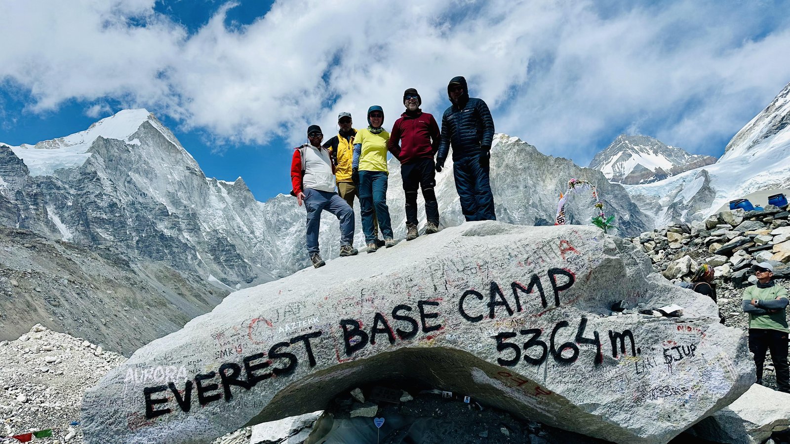 Edward and Dawn at the famous Everest Base Camp photo rock, prayer flags behind them