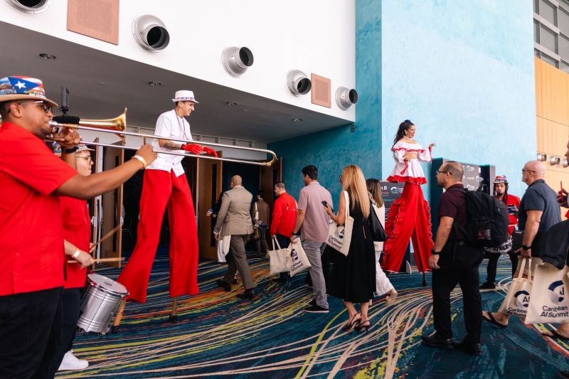A batucada band in red with a trombone and drums, plus two stilt walkers, greeting attendees as they walk in